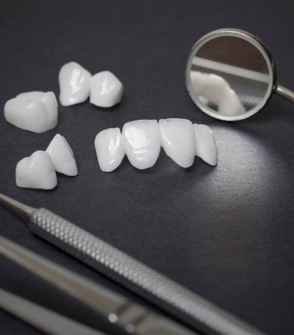 Several white dental crowns and veneers on table next to dental mirrors