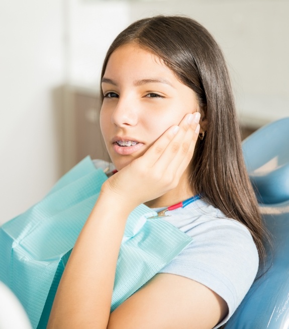 Teenage girl in dental chair holding her cheek in pain