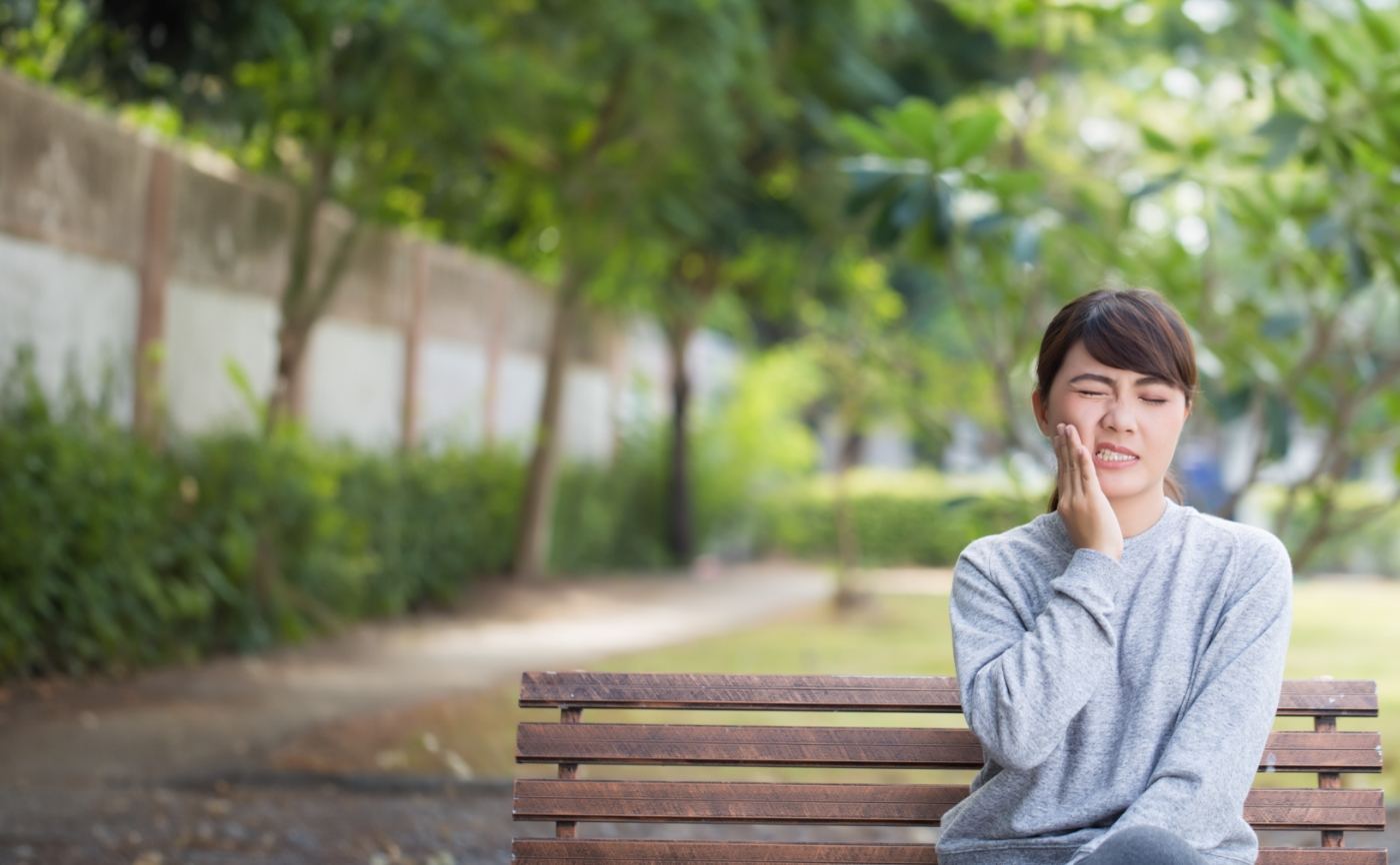 Woman on outdoor bench holding her cheek in pain needing emergency dentist in Julington Creek