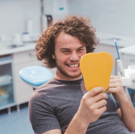 Young man in dental chair looking at his smile in a mirror