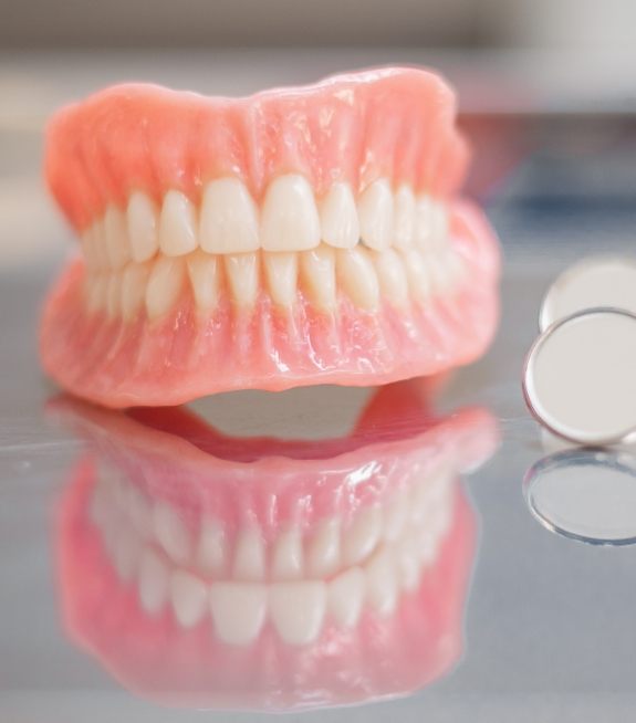 Full dentures on table next to a dental mirror