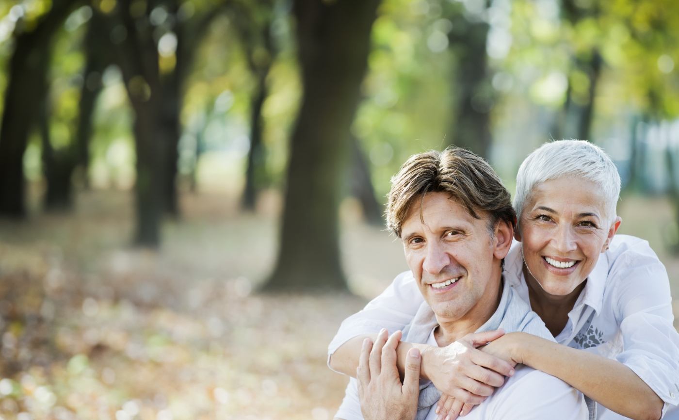 Senior man and woman smiling outdoors after replacing missing teeth in Julington Creek