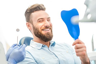 Patient smiling while holding dental mirror