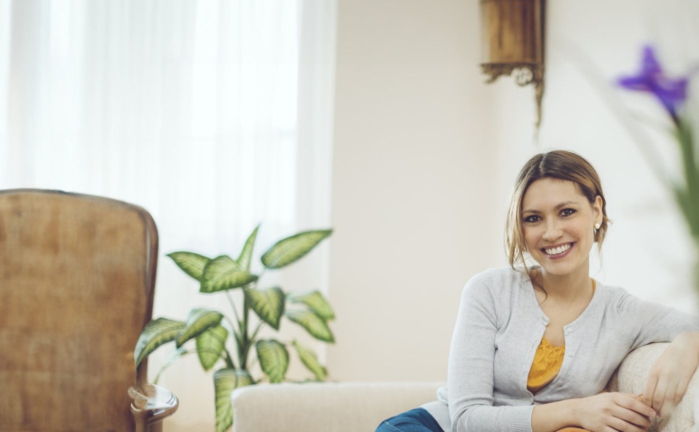 Smiling woman in white cardigan sitting on couch