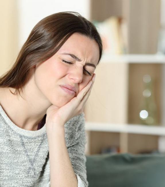 Woman sitting on couch and holding her jaw