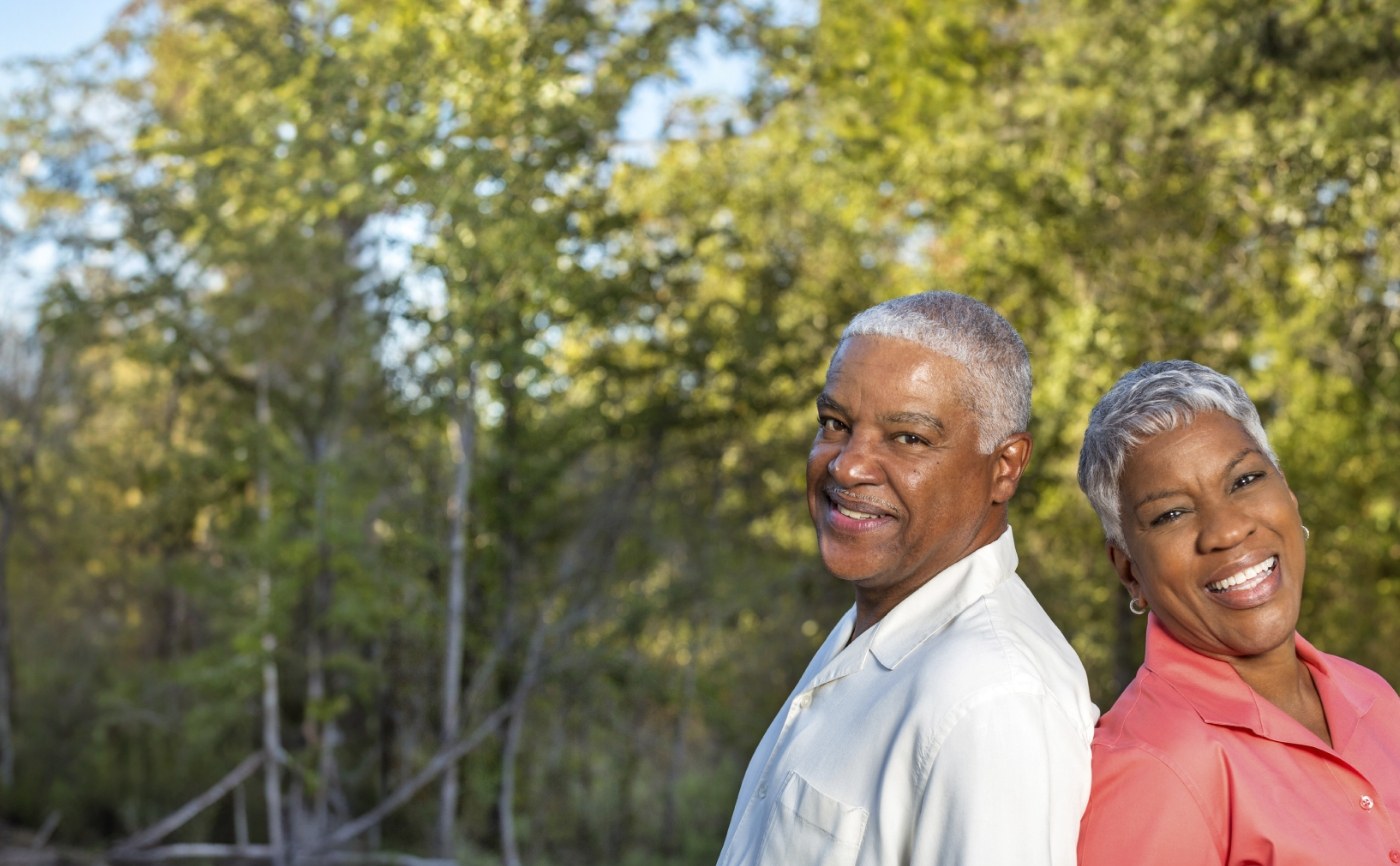 Senior man and woman smiling outdoors while standing back to back