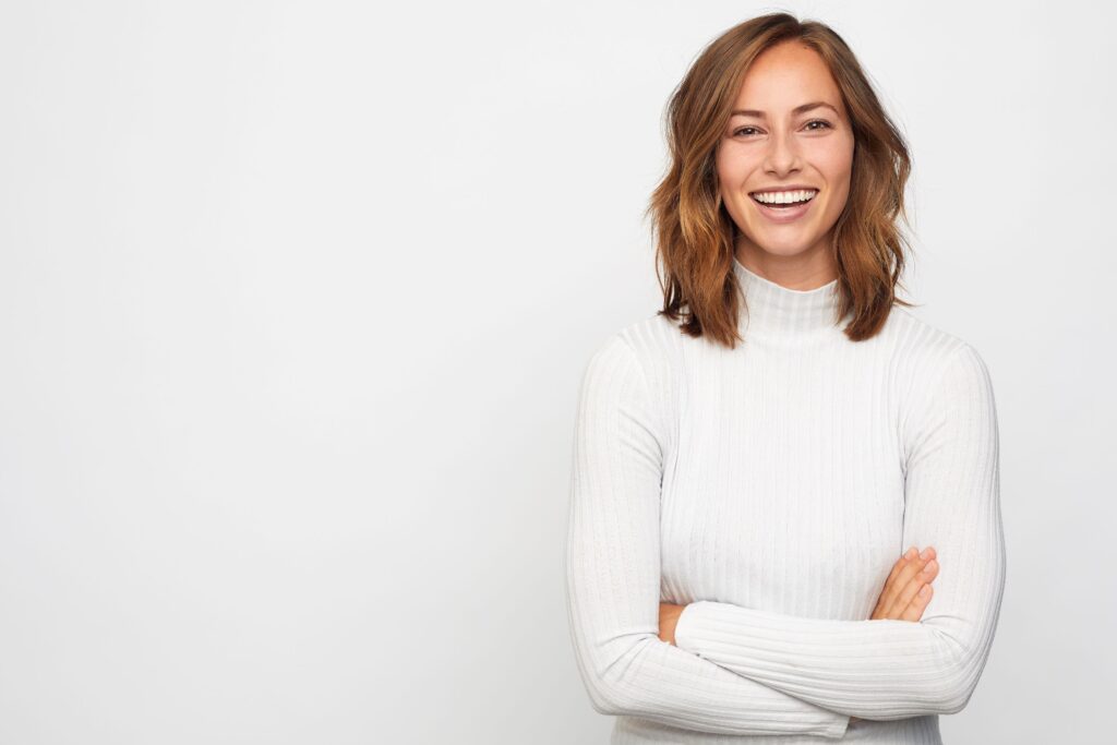 Woman with brown hair in white sweater smiling with white background